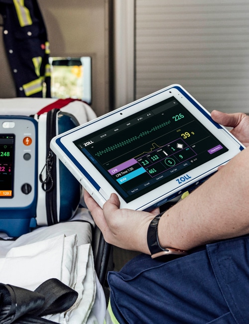 Sjukvårdspersonal sitter med en ZOLL Zenix Viewer-surfplatta i händerna bredvid en Zenix-monitor och defibrillator.